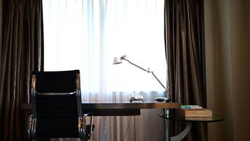 Habitación de hotel con escritorio, silla, lámpara y vistas a través de cortinas translúcidas.