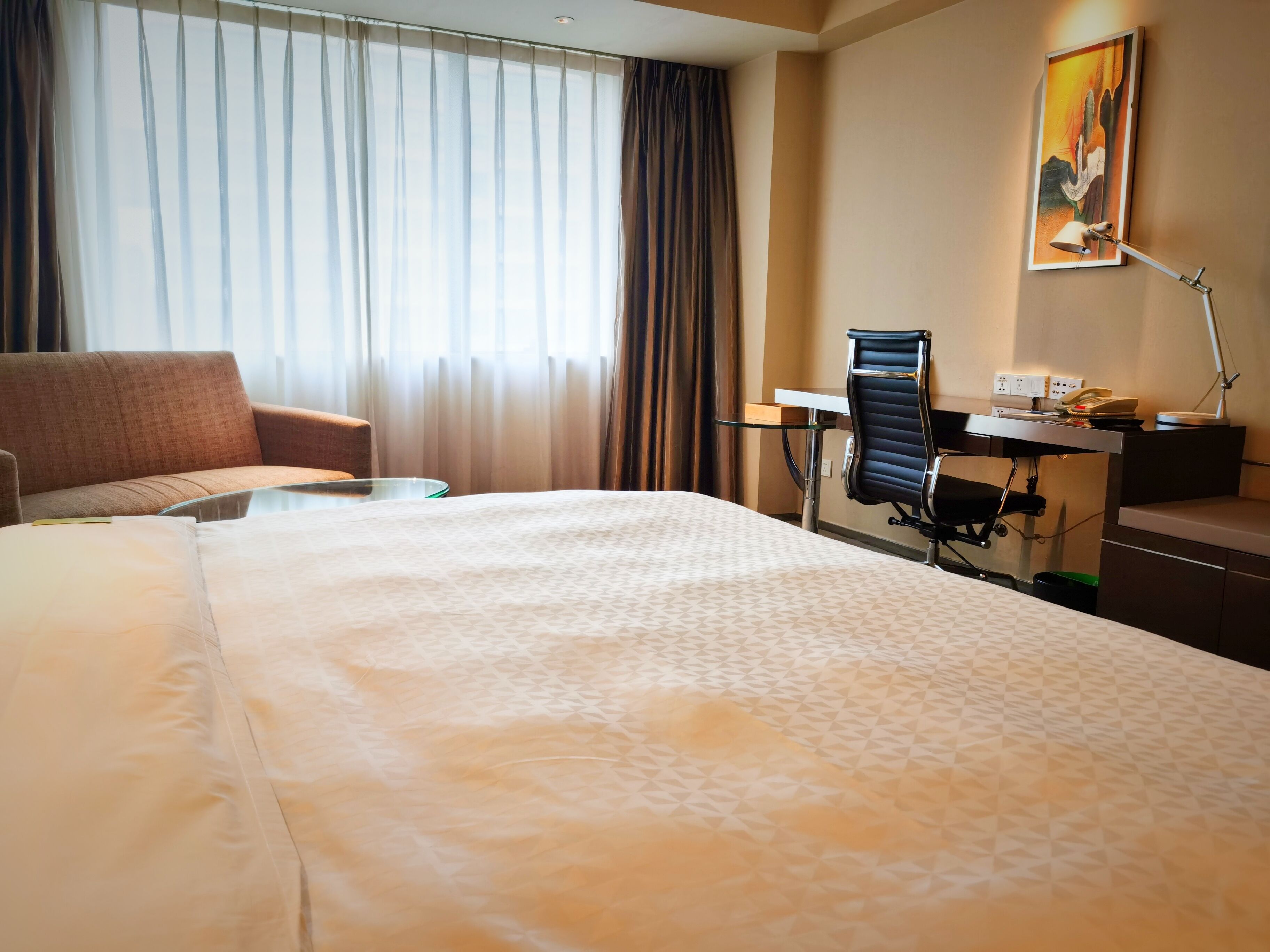 Une chambre d’hôtel avec un grand lit, un bureau, une chaise et une fenêtre avec des rideaux.