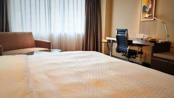 Une chambre d’hôtel avec un grand lit, un bureau, une chaise et une fenêtre avec des rideaux.