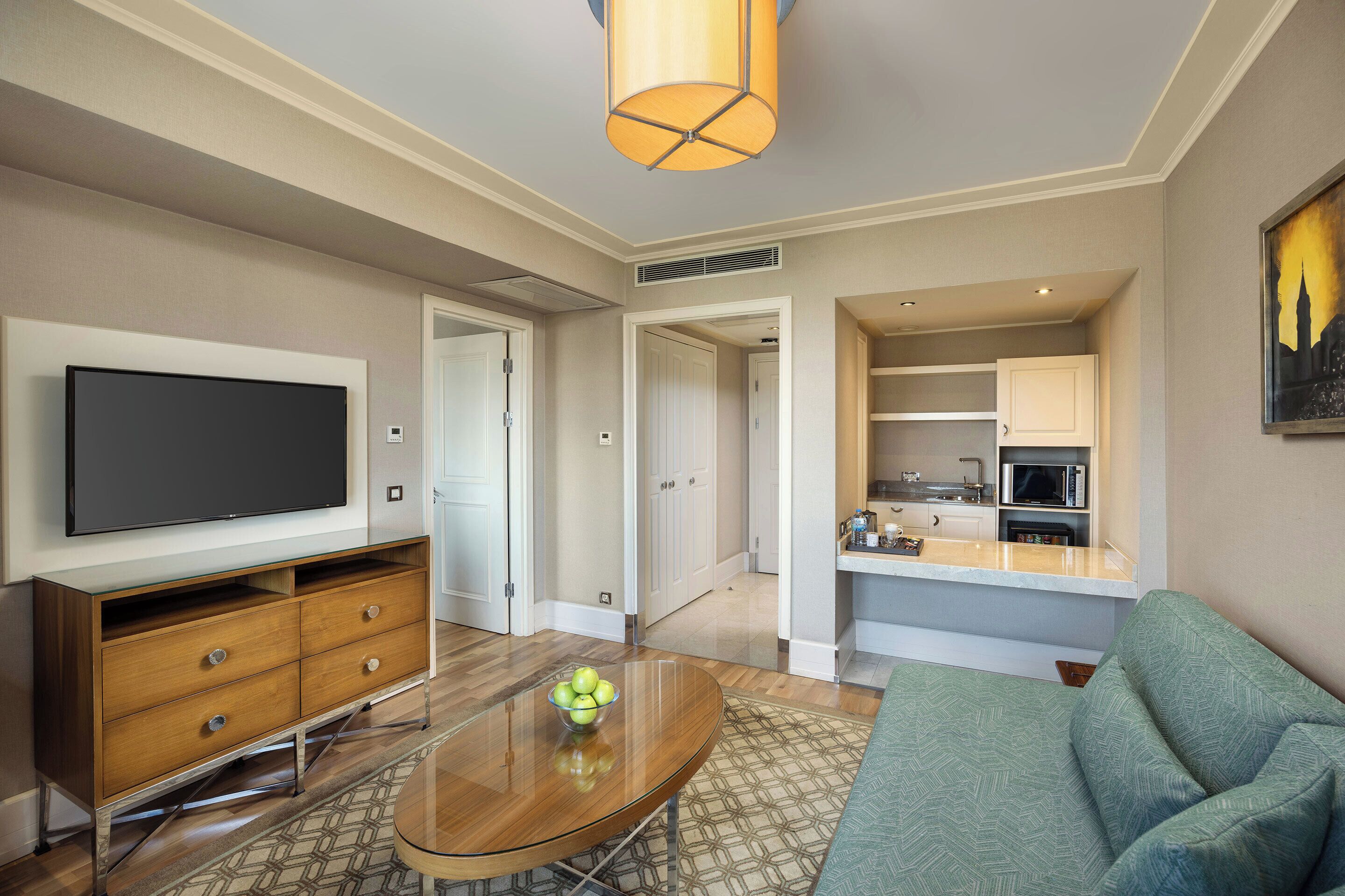 A modern living room with a flat-screen TV, wooden entertainment unit, and a glass coffee table with a bowl of fruit.
