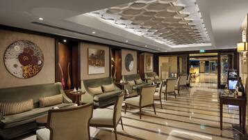 Un hall d’hôtel au design moderne, comprenant un espace salon avec des canapés et des fauteuils, un sol à motifs et des panneaux décoratifs au plafond.