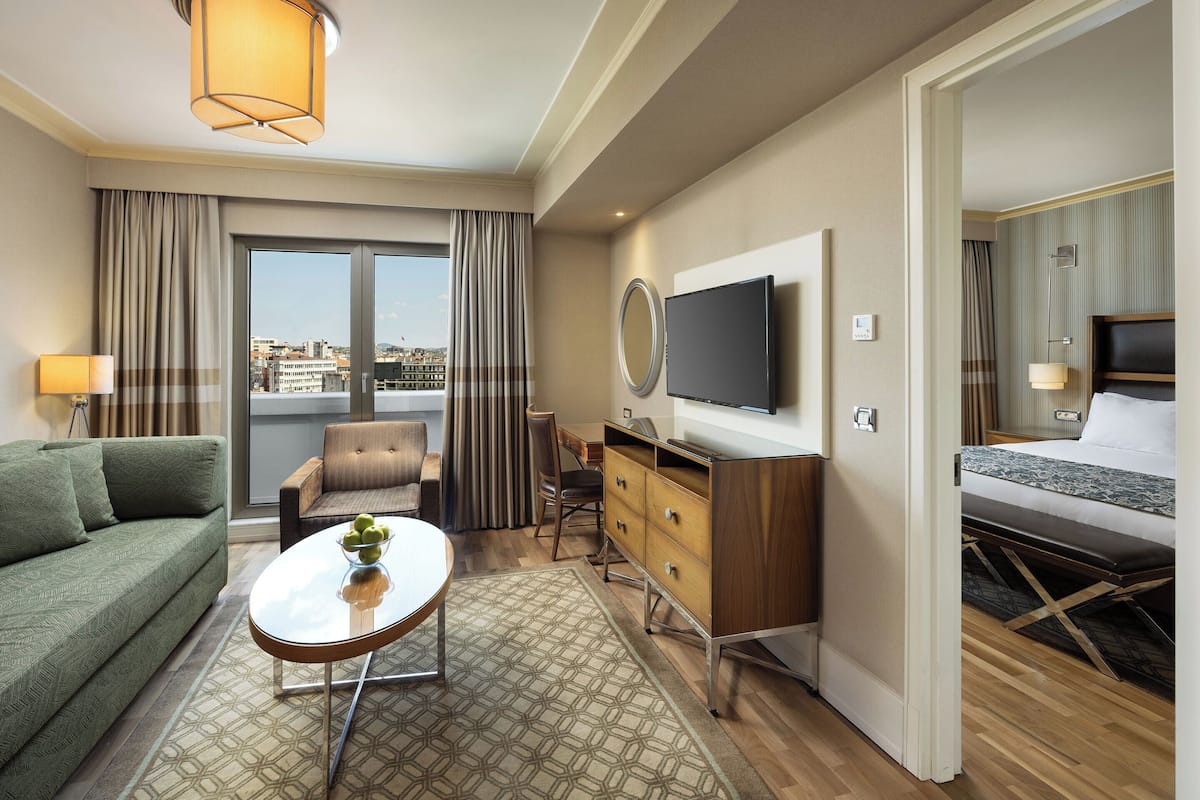 Habitación de hotel con sofá, una mesita con un frutero, cómoda de madera, televisor y cama.