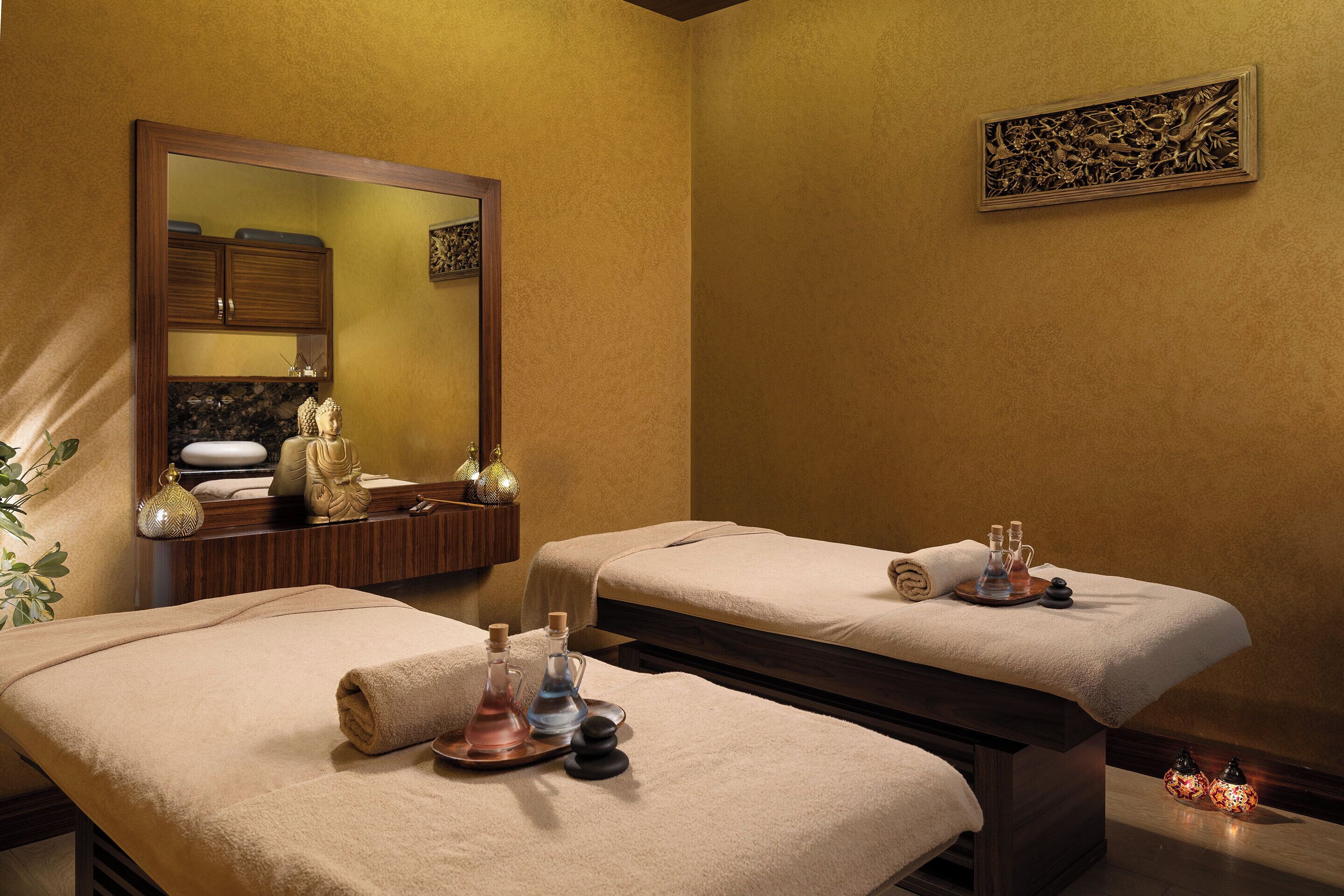 Une salle de spa équipée de deux tables de massage, chacune ayant une serviette et un plateau avec des bouteilles.
