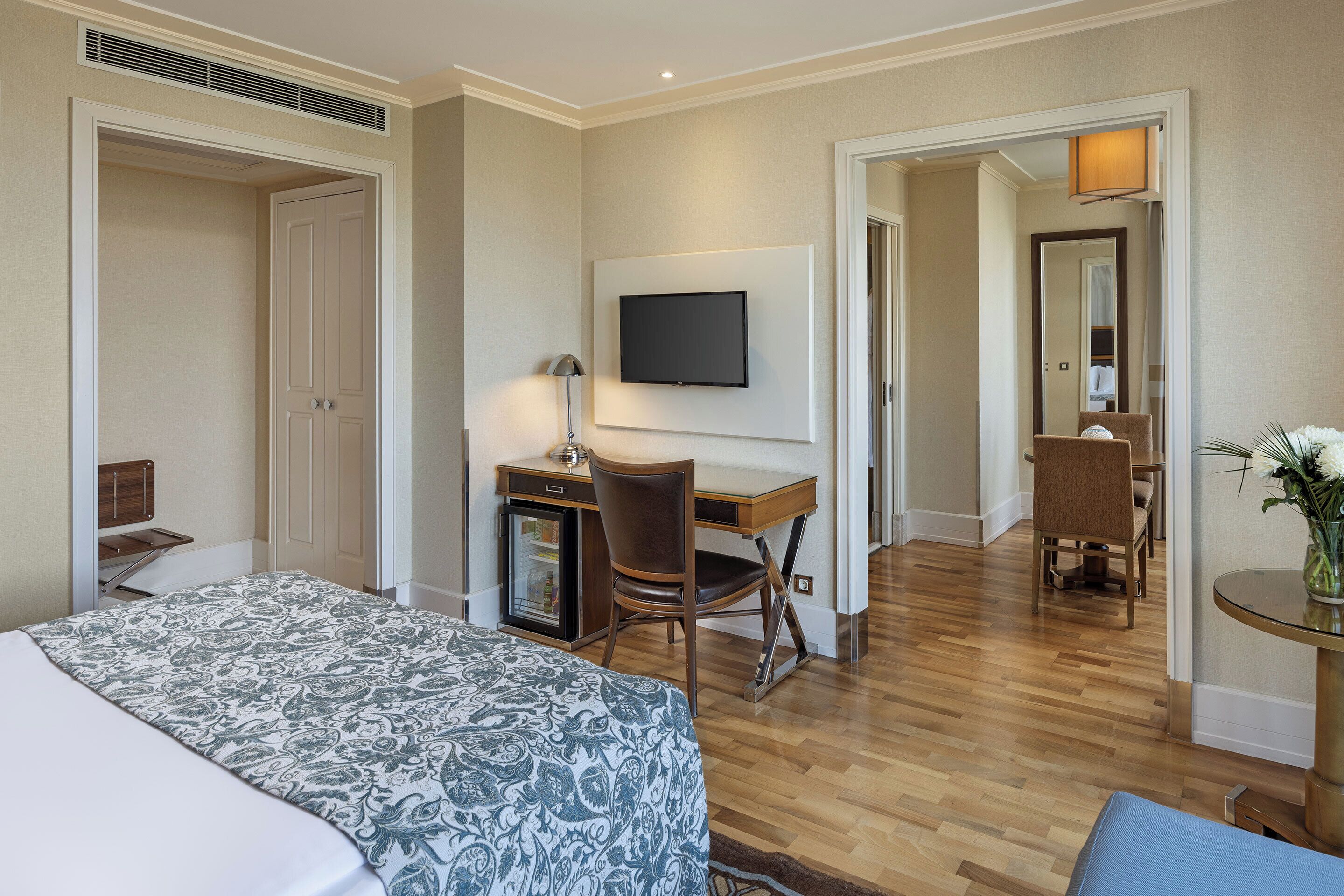 A hotel room with a bed, a desk with a chair, a television, and a small table with a plant.