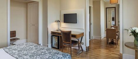 A hotel room with a bed, a desk with a chair, a television, and a small table with a plant.
