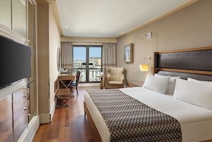 A hotel room with a large bed, a desk, a chair, and a TV.
