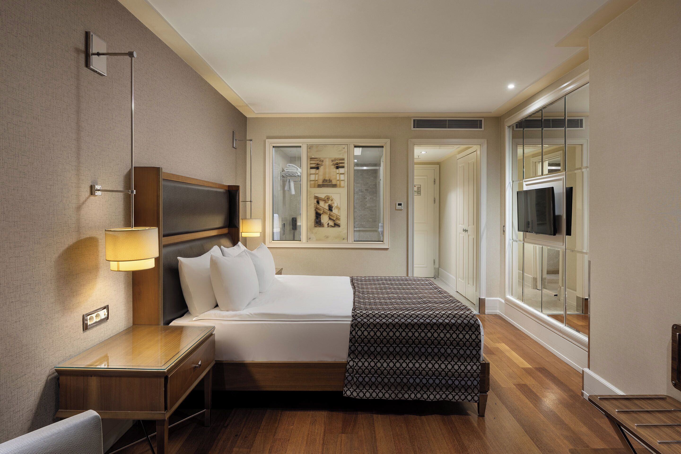 A hotel room with a bed, bedside table, lamp, and a large window.