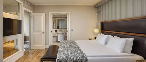 Une chambre d’hôtel avec un grand lit, un banc, une télévision et une salle de bain visible à travers une porte ouverte.