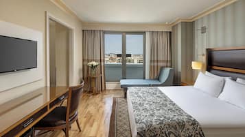 Ein Hotelzimmer mit einem großen Bett, einem Schreibtisch mit Stuhl, einem Fernseher und Blick auf die Stadt durch das Fenster.