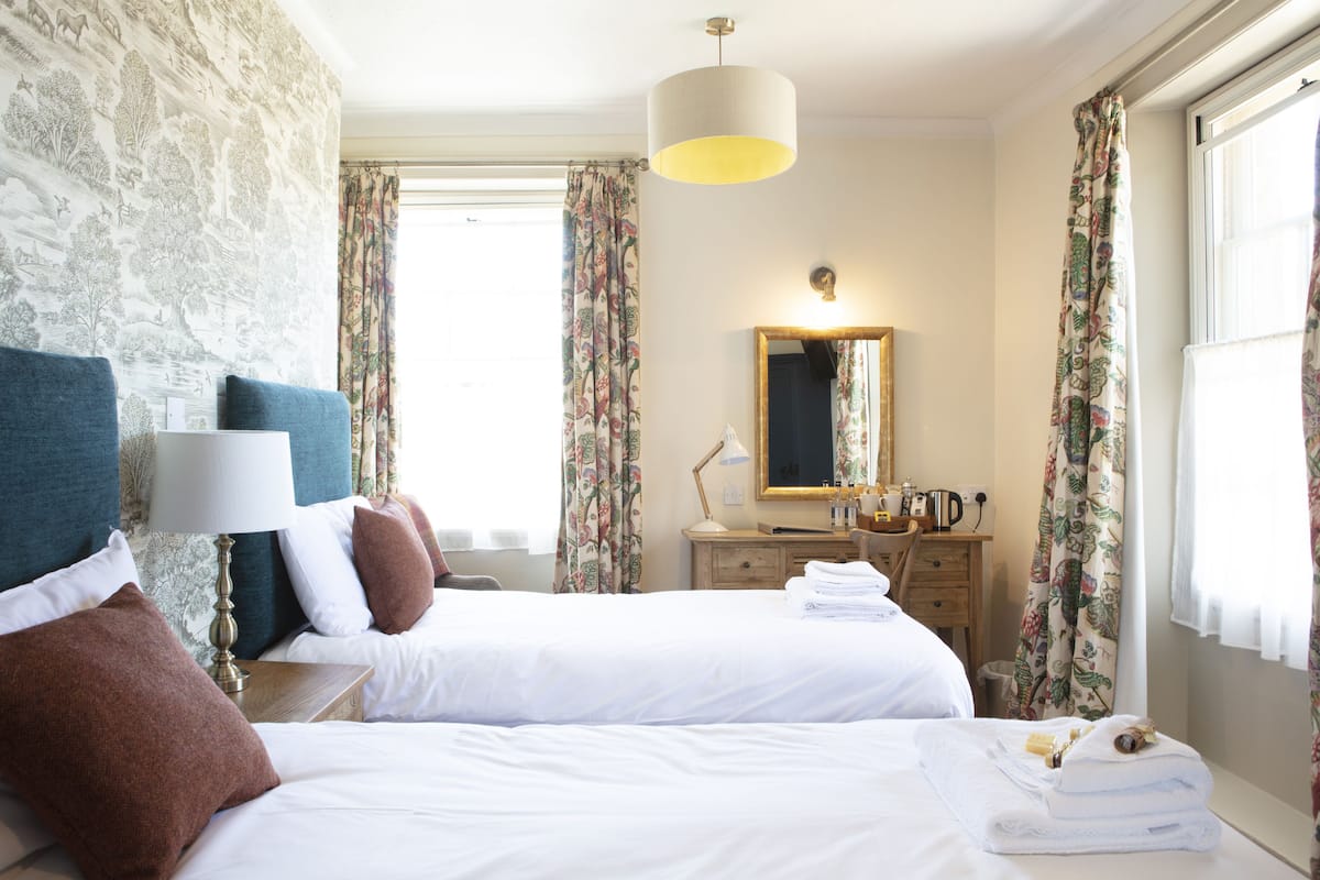 Habitación de hotel con dos camas, un espejo, una cómoda y una ventana con cortinas.