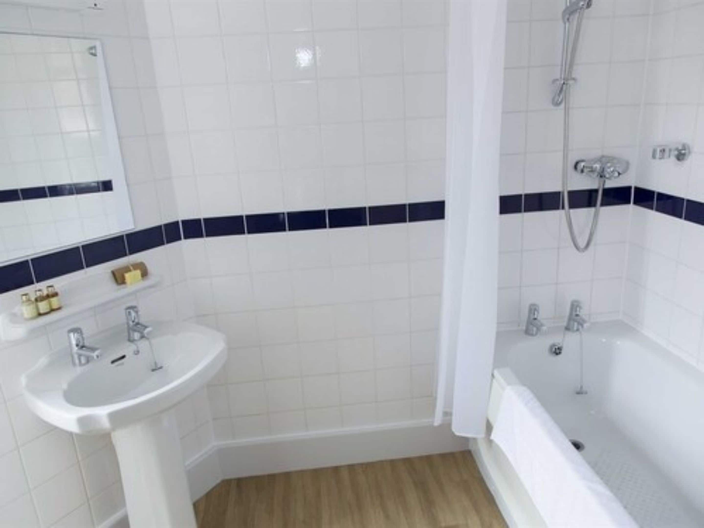 Une salle de bain avec des carreaux blancs, un lavabo, une baignoire et une douche.