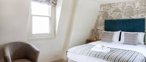 A bedroom with a bed, a chair, a window with a floral valance, and a stone-patterned wall.