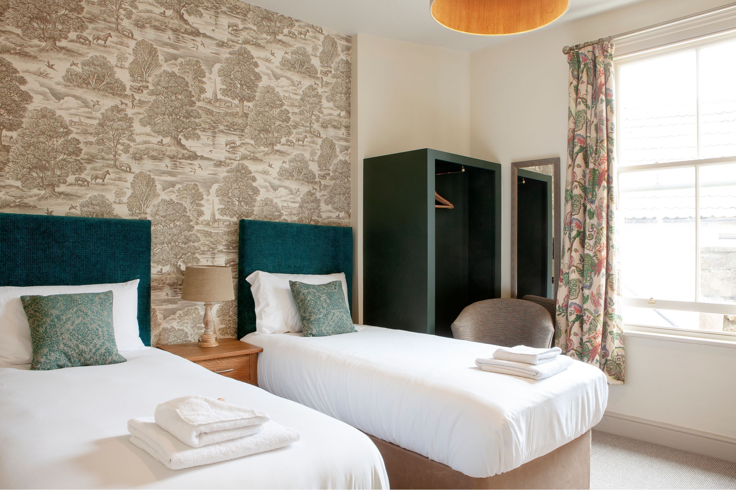 Una habitación de hotel con dos camas, un ventanal con cortinas, un armario y un espejo.