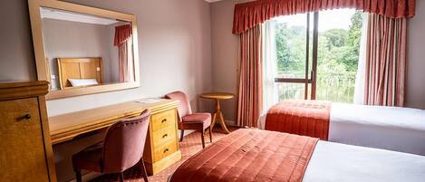 A hotel room with a bed, a desk, a chair, a dresser, a mirror, and a window with curtains.