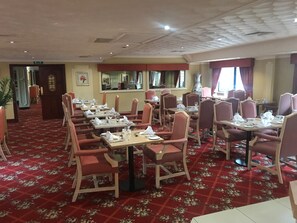 Ein Restaurant mit rotem Teppich, floralem Muster, Holzkästen und Tischen, gedeckt mit weißen Tischdecken und Servietten.