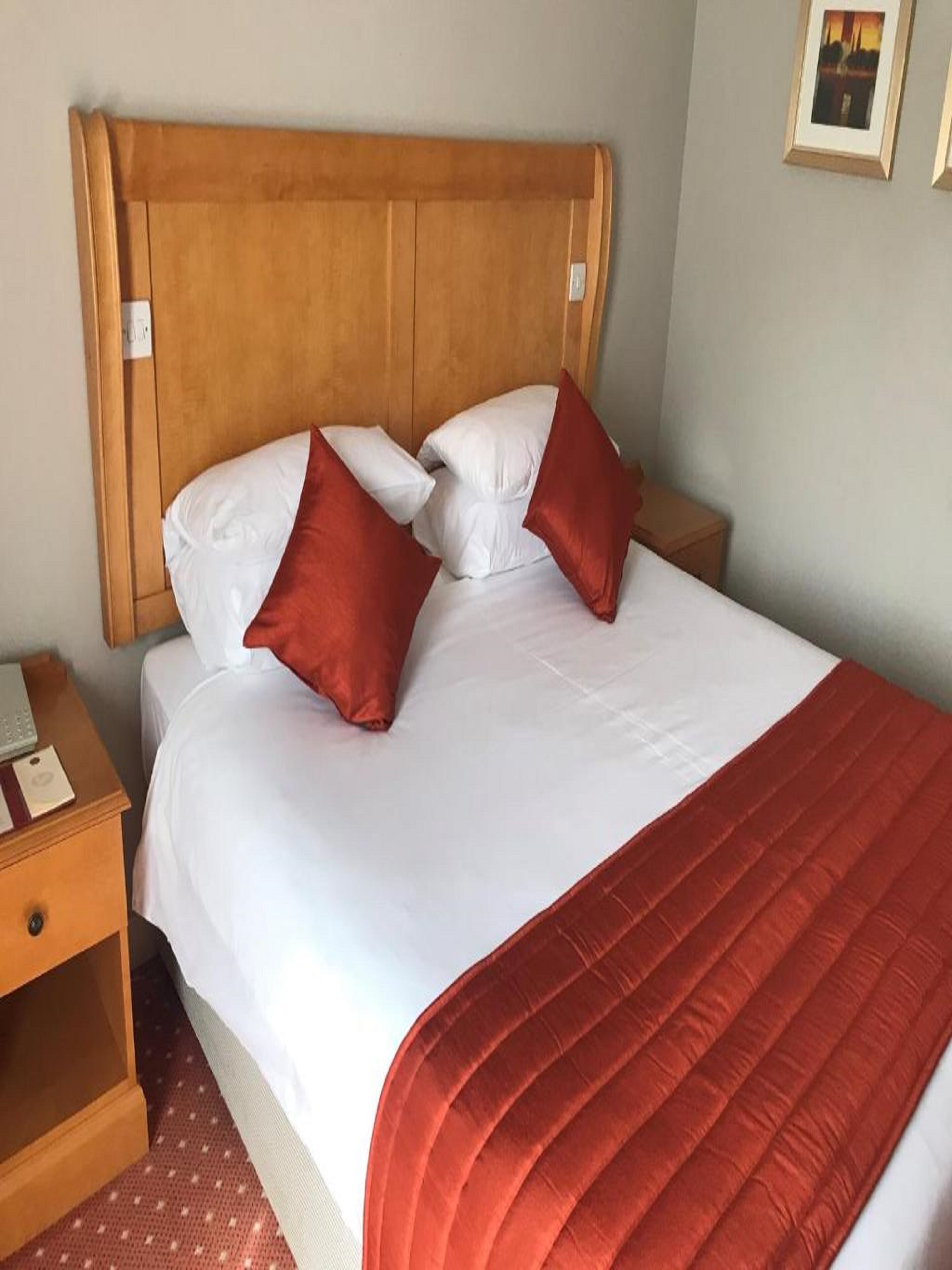 A neatly made bed with a wooden headboard, white bedding, and two red pillows.