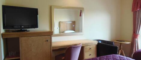 Une chambre d’hôtel comprenant un lit, un bureau avec une chaise, une télévision, un miroir et une petite table.