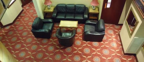 A hotel lobby with a red patterned carpet, a black leather sofa set, two armchairs, a small wooden coffee table, and framed artwork on the wall.