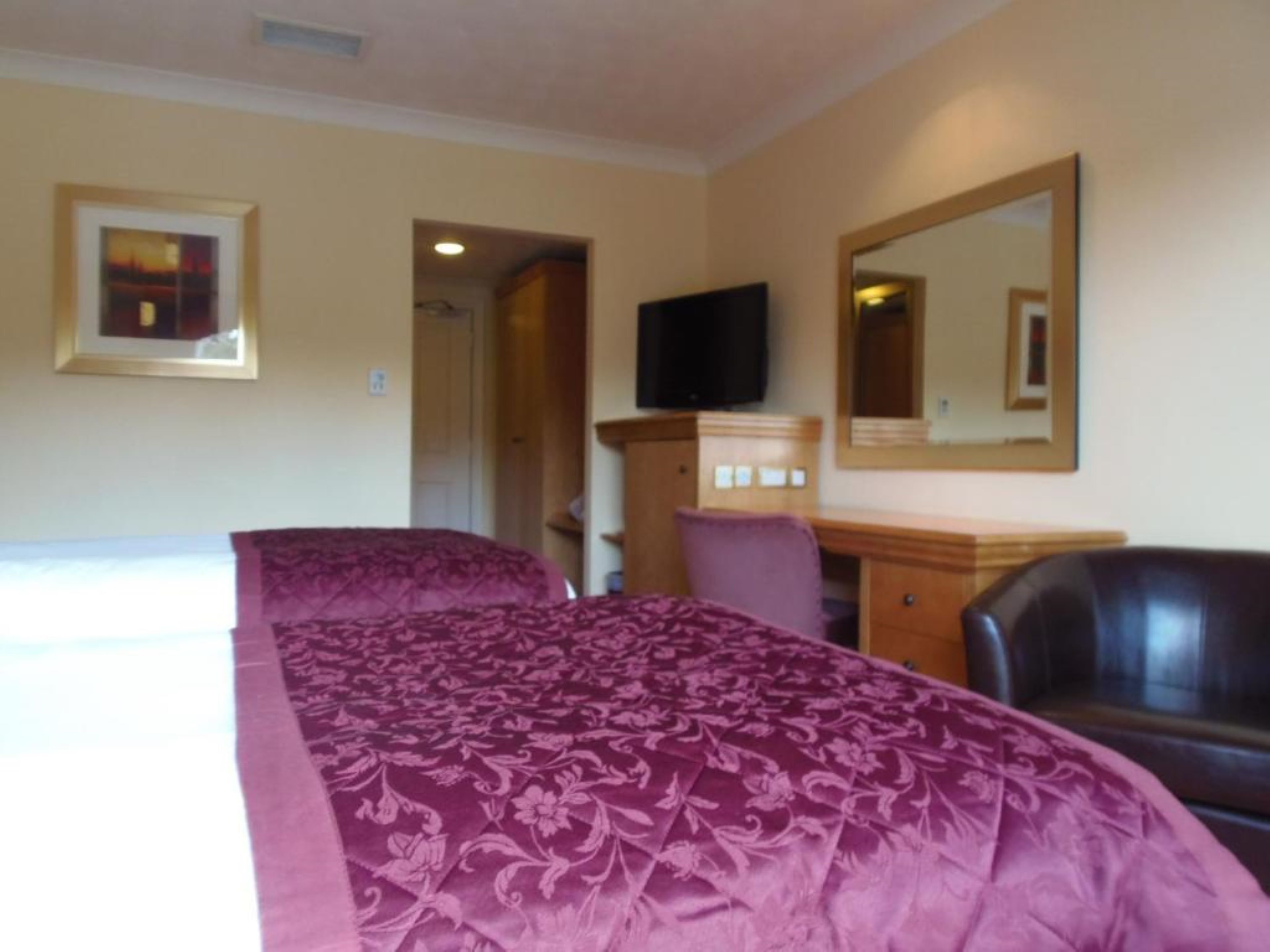 A hotel room with a bed, a desk, a chair, a television, and a mirror.