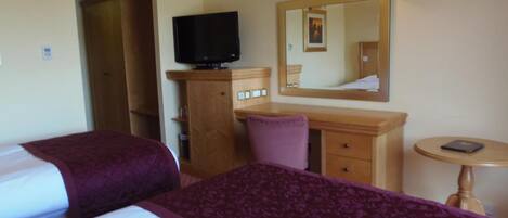 A hotel room with two beds, a television, a desk with a chair, a small table, and a mirror.