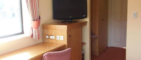 Ein Zimmer mit Holzschreibtisch, Fernseher, rosa Stuhl und einem Bett mit gemustertem Überwurf.