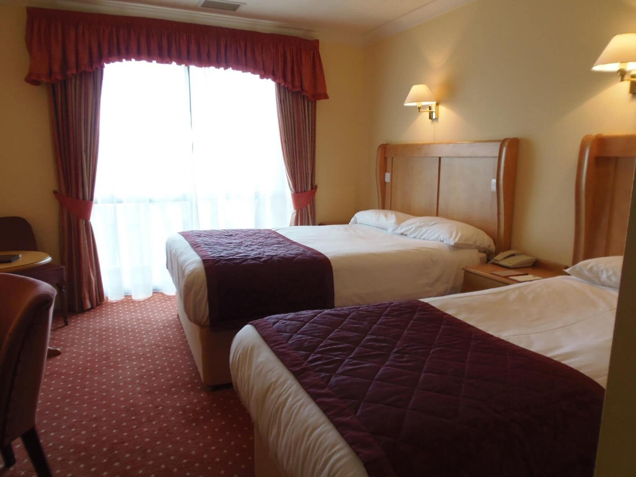 Quarto de hotel com duas camas, uma escrivaninha e uma cadeira.