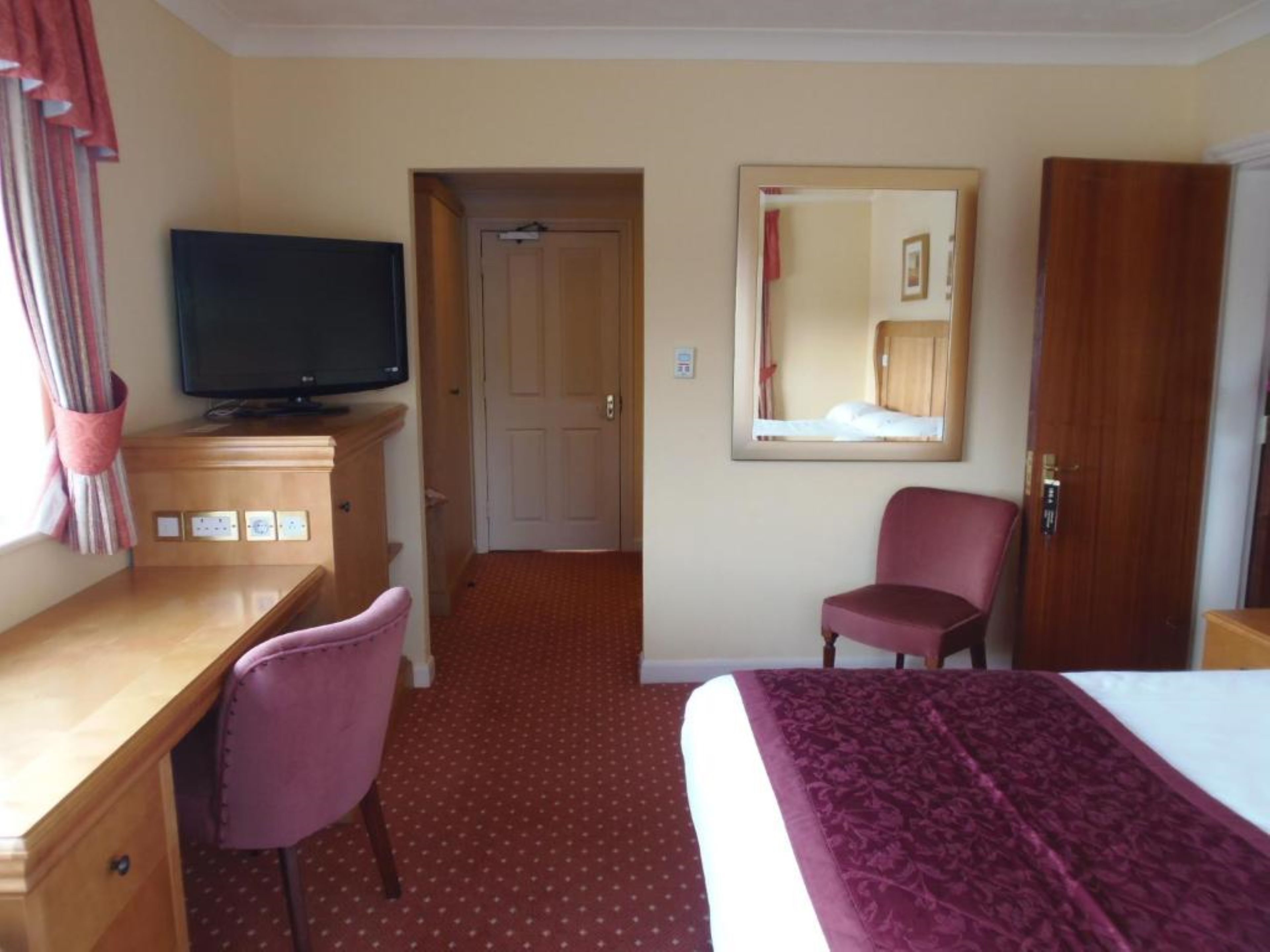 Une chambre d’hôtel avec un lit, un bureau et une chaise, une télévision et un miroir au mur.