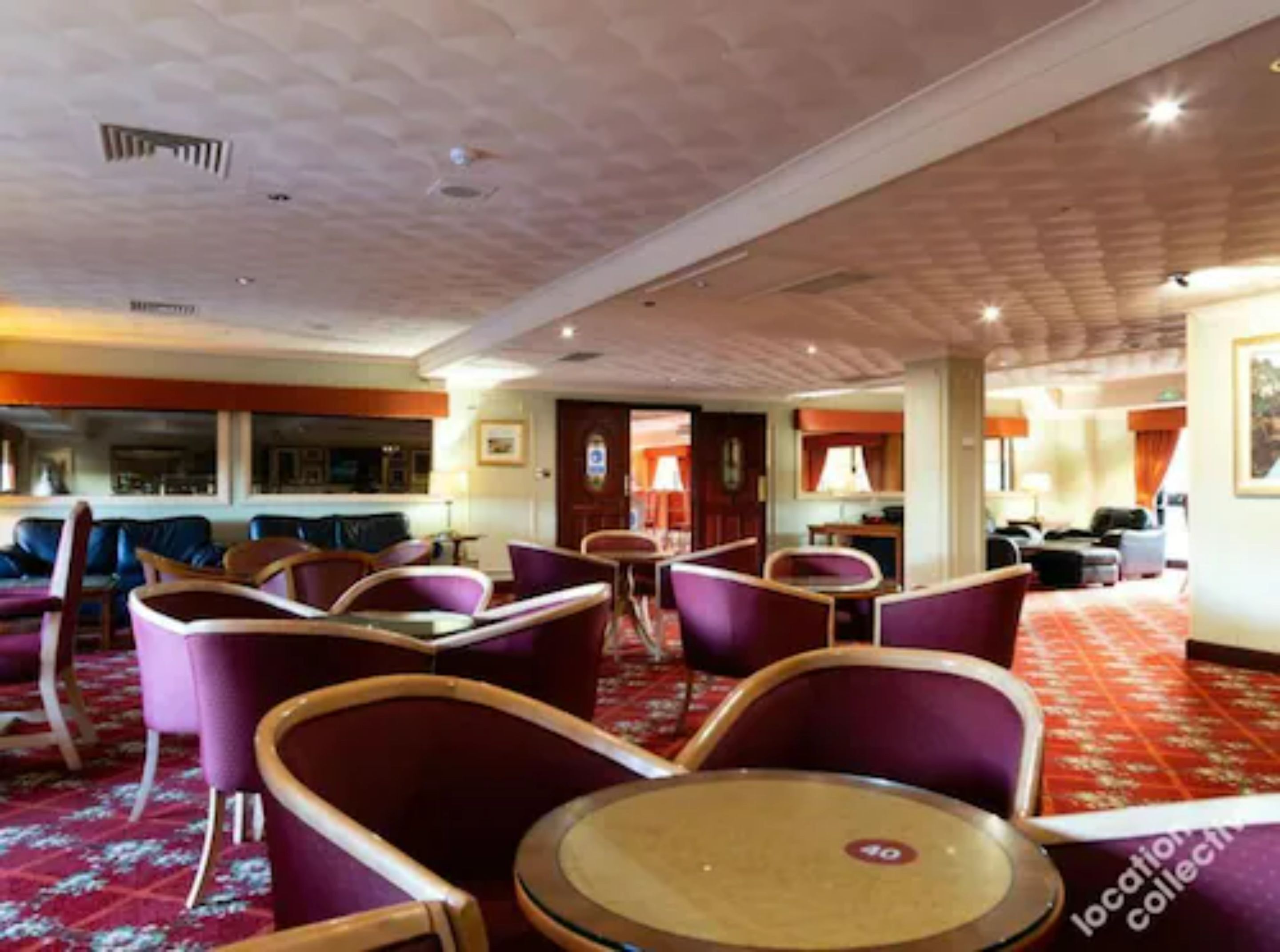 A hotel lobby with purple seating, a red carpet, and a location collection sign.