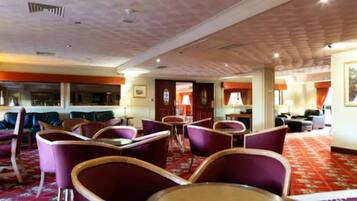 Hall d'albergo con sedute viola, tappeto rosso e cartello indicazioni.