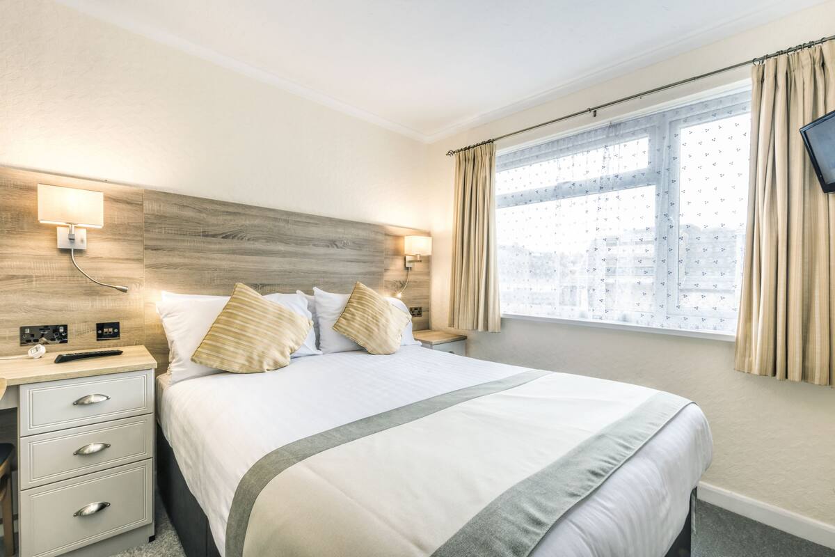 A hotel room with a large bed, bedside tables, a flat-screen TV, and a window with curtains.