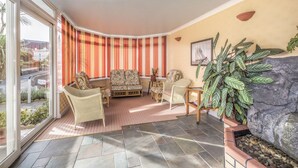 A corner living room with a sofa, chairs, a table, and a large plant. - Lindum Lodge (Torquay)
