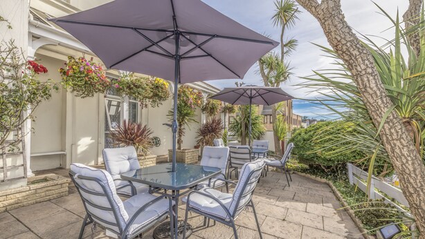 An outdoor patio with a glass table and chairs, surrounded by potted plants and umbrellas. - Lindum Lodge (Torquay)