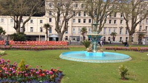 A well-maintained garden with a central fountain, surrounded by colorful flower beds and a large building in the background. - Lindum Lodge (Torquay)