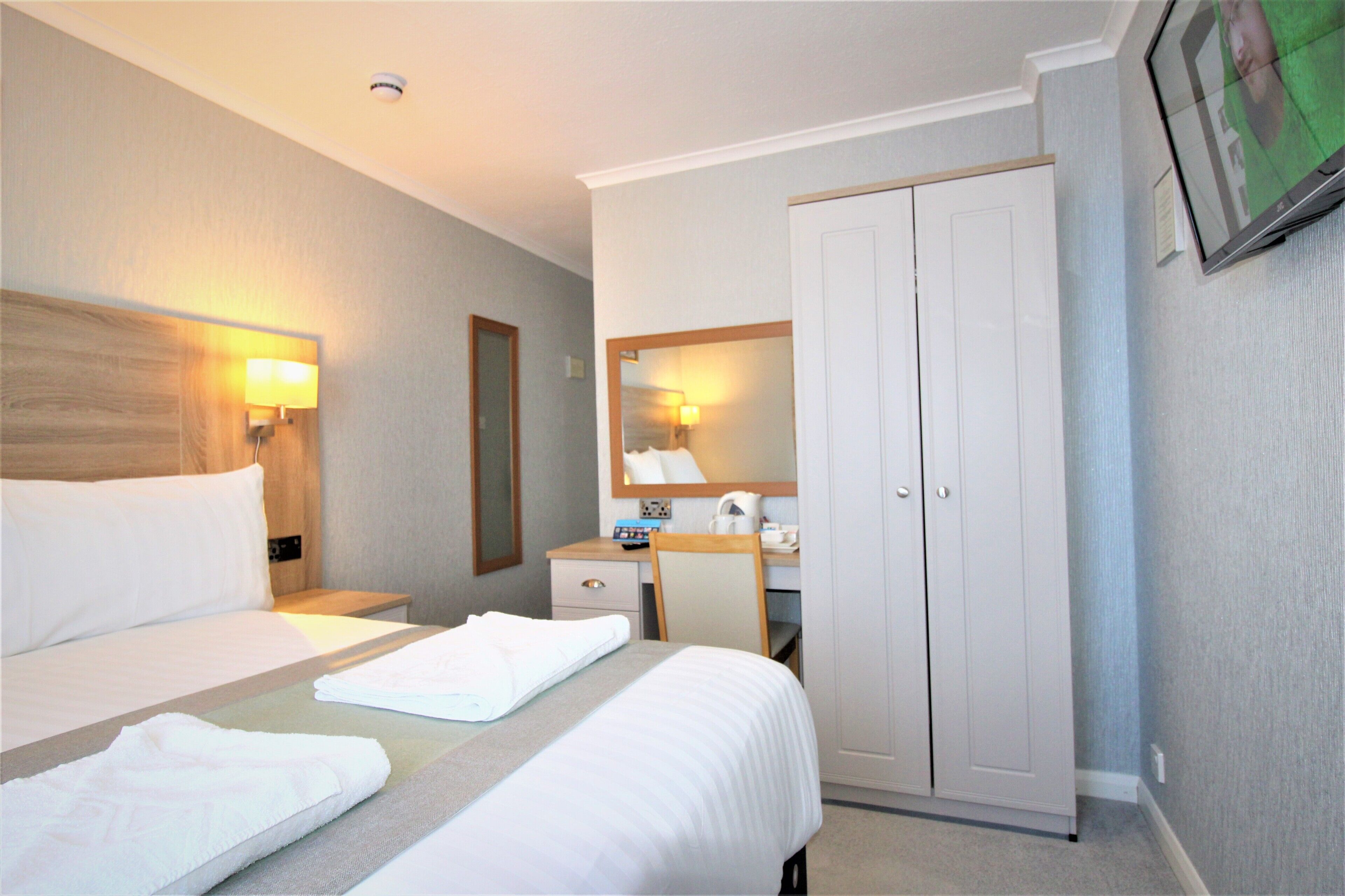A hotel room with a bed, a desk, a chair, a wardrobe, and a TV mounted on the wall.