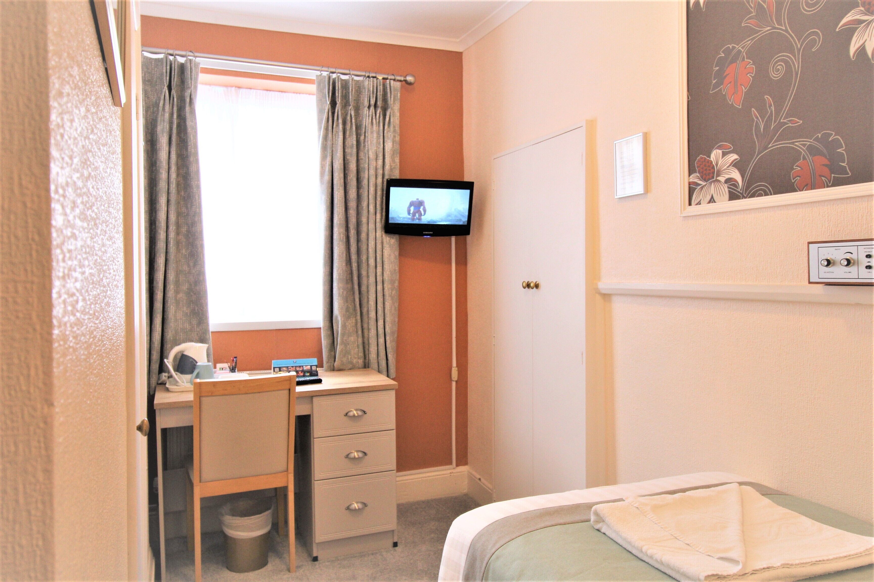 A bedroom with a bed, a desk with a chair, a television, and a window with curtains.