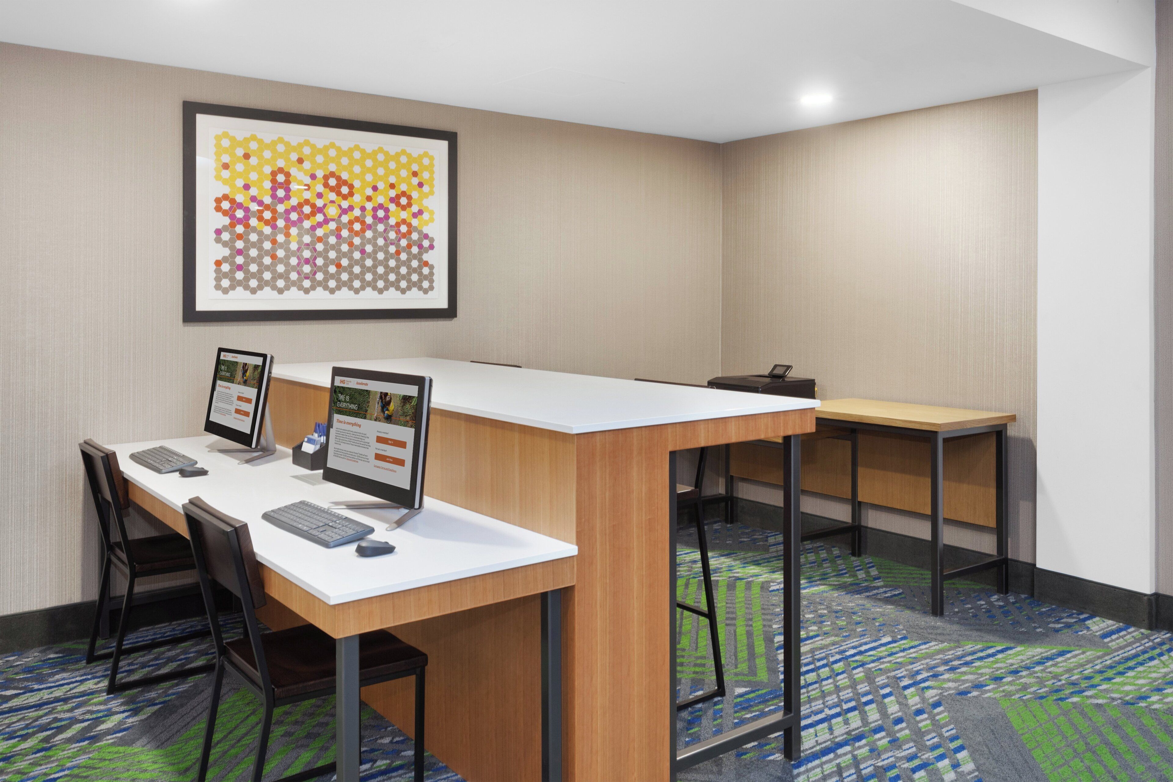 A conference room with a long table, two chairs, a computer, and a framed artwork on the wall.