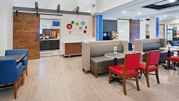A modern restaurant with a breakfast counter, seating areas with red and grey chairs, and a wall decorated with plates. - Holiday Inn Express Hotel & Suites Culpeper by IHG (Culpeper)