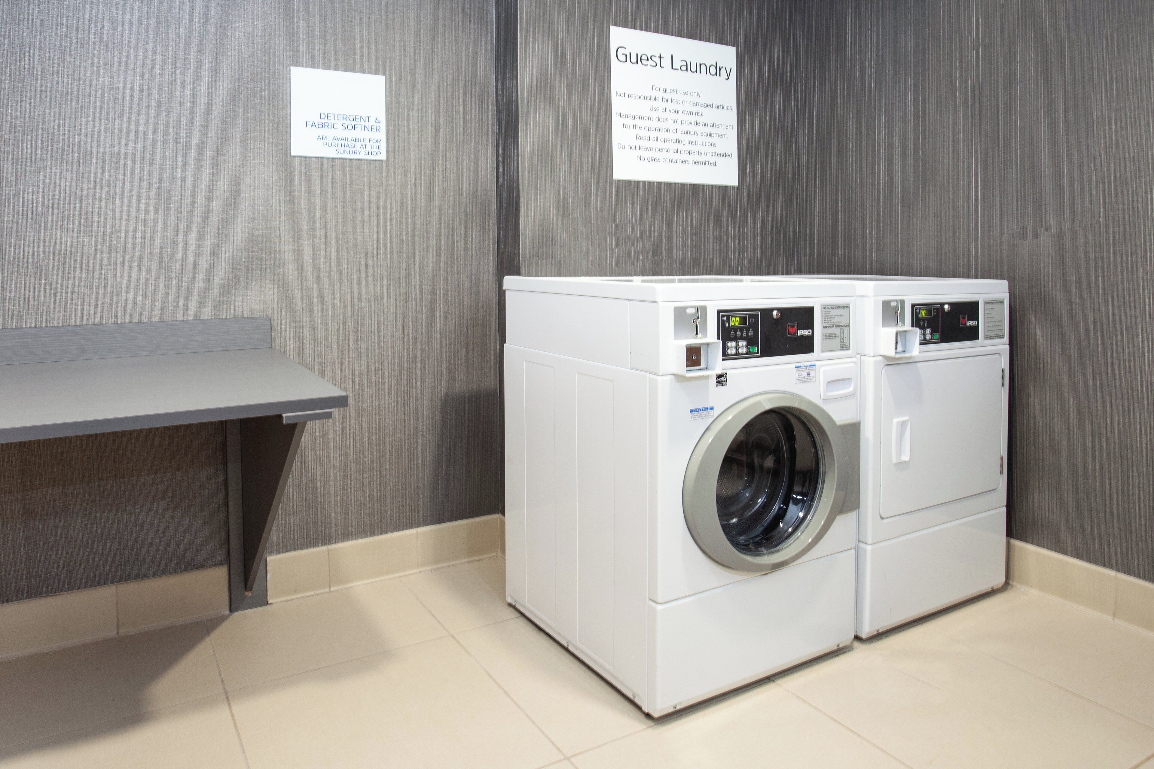 A guest laundry area with a front-loading washing machine, a bench, and two informational signs.