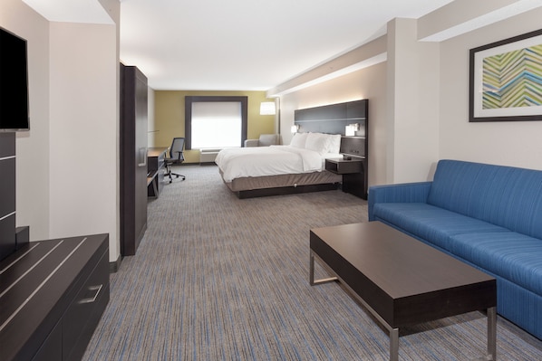 A hotel room with a bed, a blue sofa, a desk, a TV, and a framed picture on the wall.