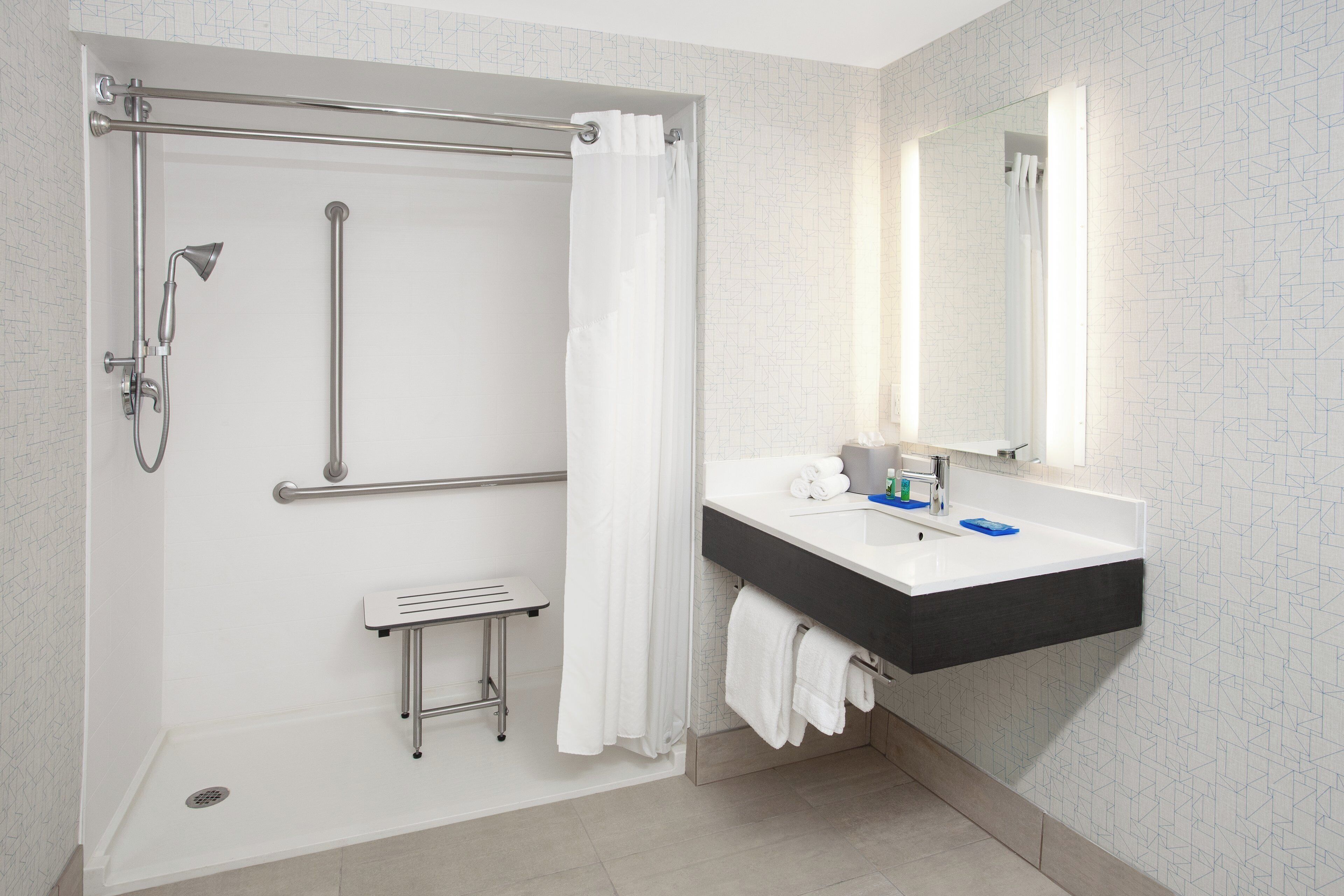 A modern bathroom with a walk-in shower, grab bar, and a sink with a mirror.
