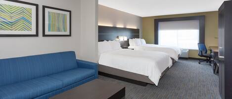 A hotel room with a bed, a blue sofa, a coffee table, and two framed artworks on the wall.