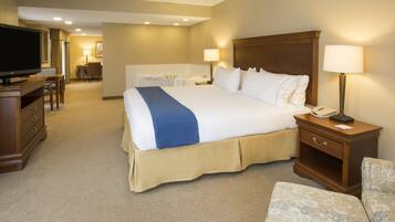 A hotel room with a large bed, a desk, a chair, a television, and a bathroom in the background.