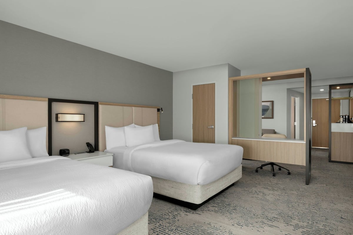 A hotel room with two beds, a desk, a chair, a mirror, and a wardrobe.