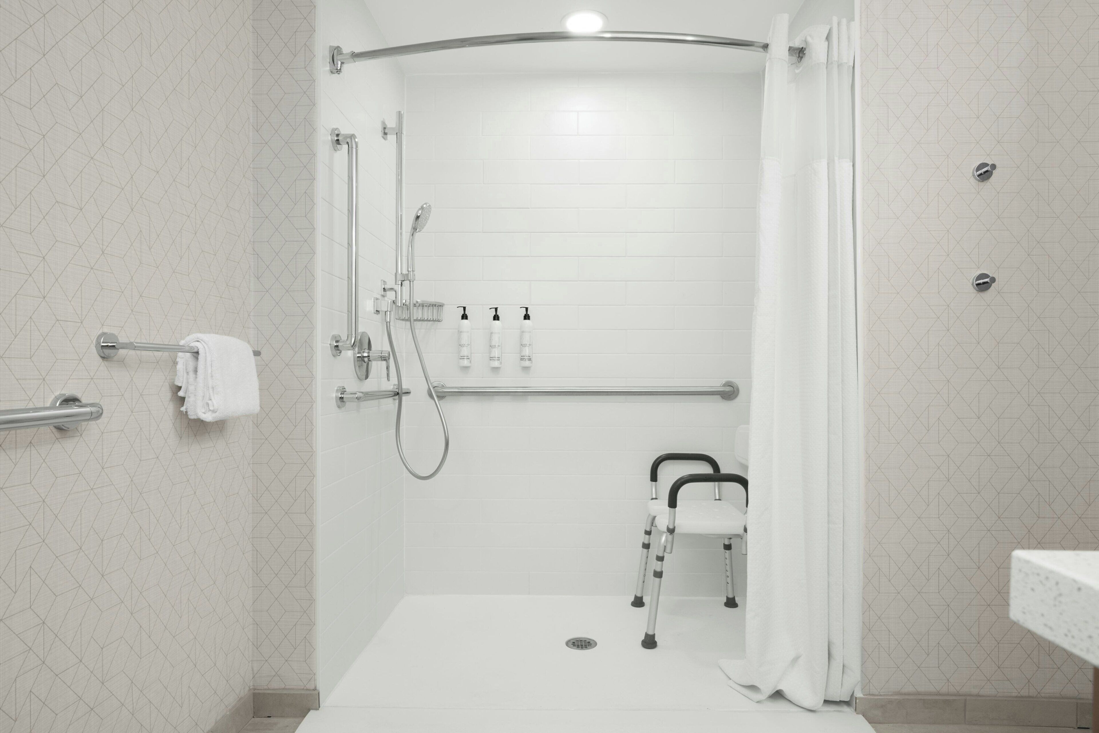 A shower area with a grab bar, a wheelchair, and a towel rack.