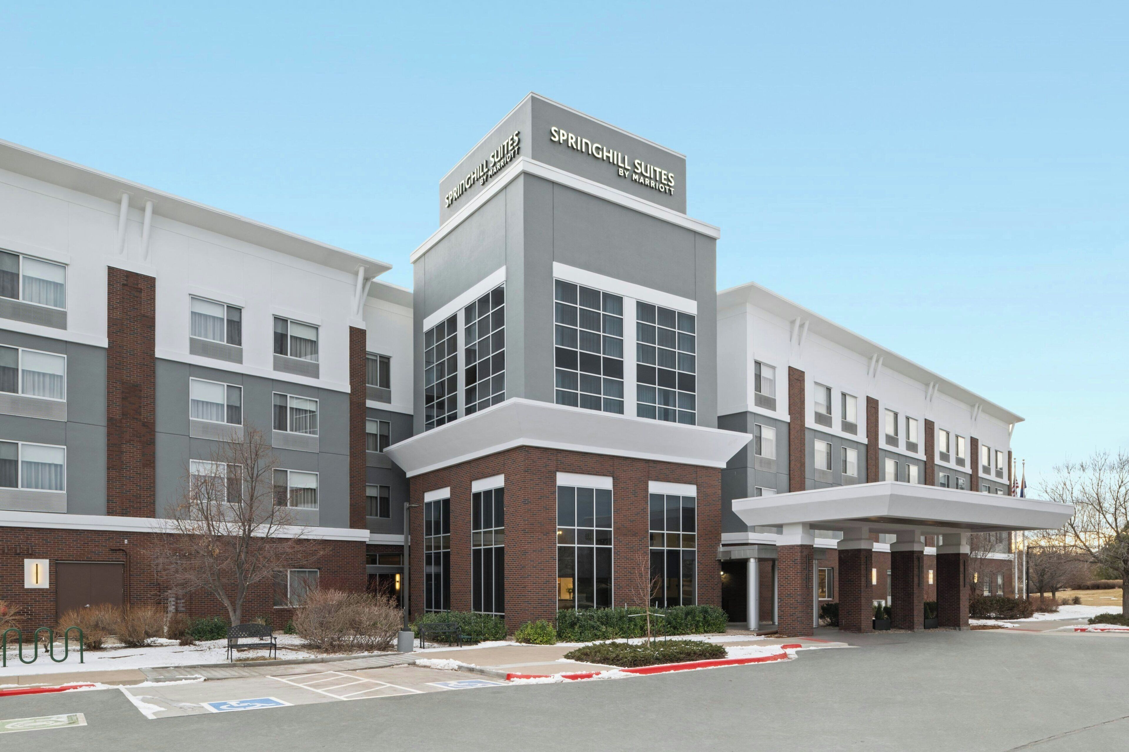 A modern hotel with a prominent 'SPRINGHILL SUITES' sign, a covered entrance, and a parking lot with marked spaces.