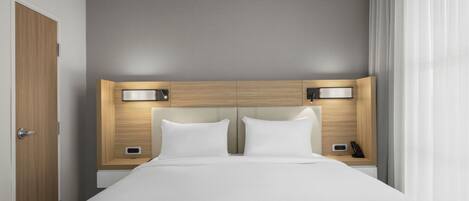 A hotel room with a large bed, two bedside tables with lamps, a wooden headboard, and a door.