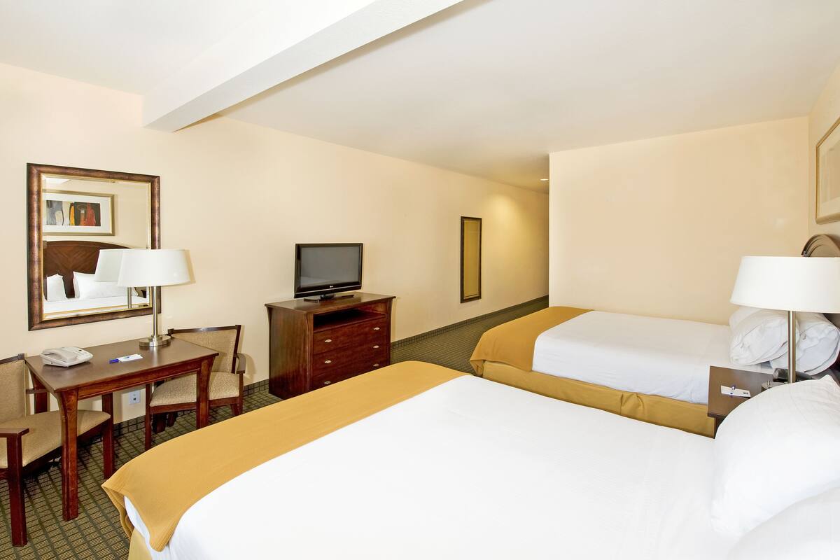 A hotel room with two beds, a desk, a television, and a mirror.