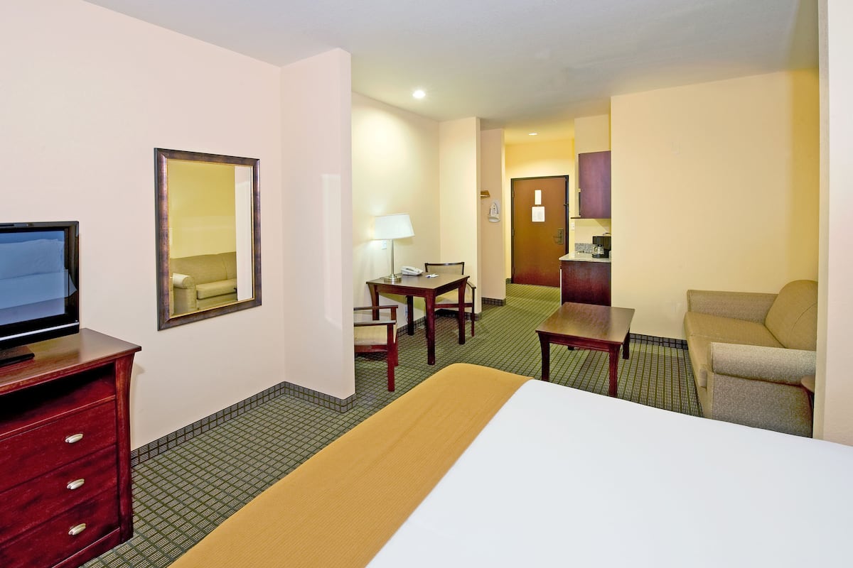 A hotel room with a bed, a desk, a chair, a TV, and a mirror.