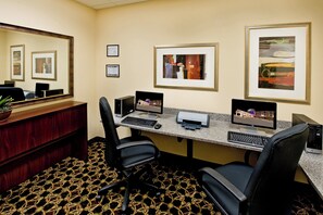 Een hotelkantoor met twee computers, een printer, een bureau, stoelen, een bureaulamp en ingelijste foto's aan de muur.