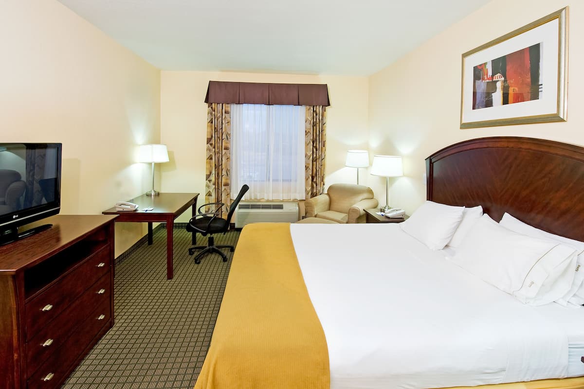 A hotel room with a bed, a desk, a television, a chair, and a window with curtains.